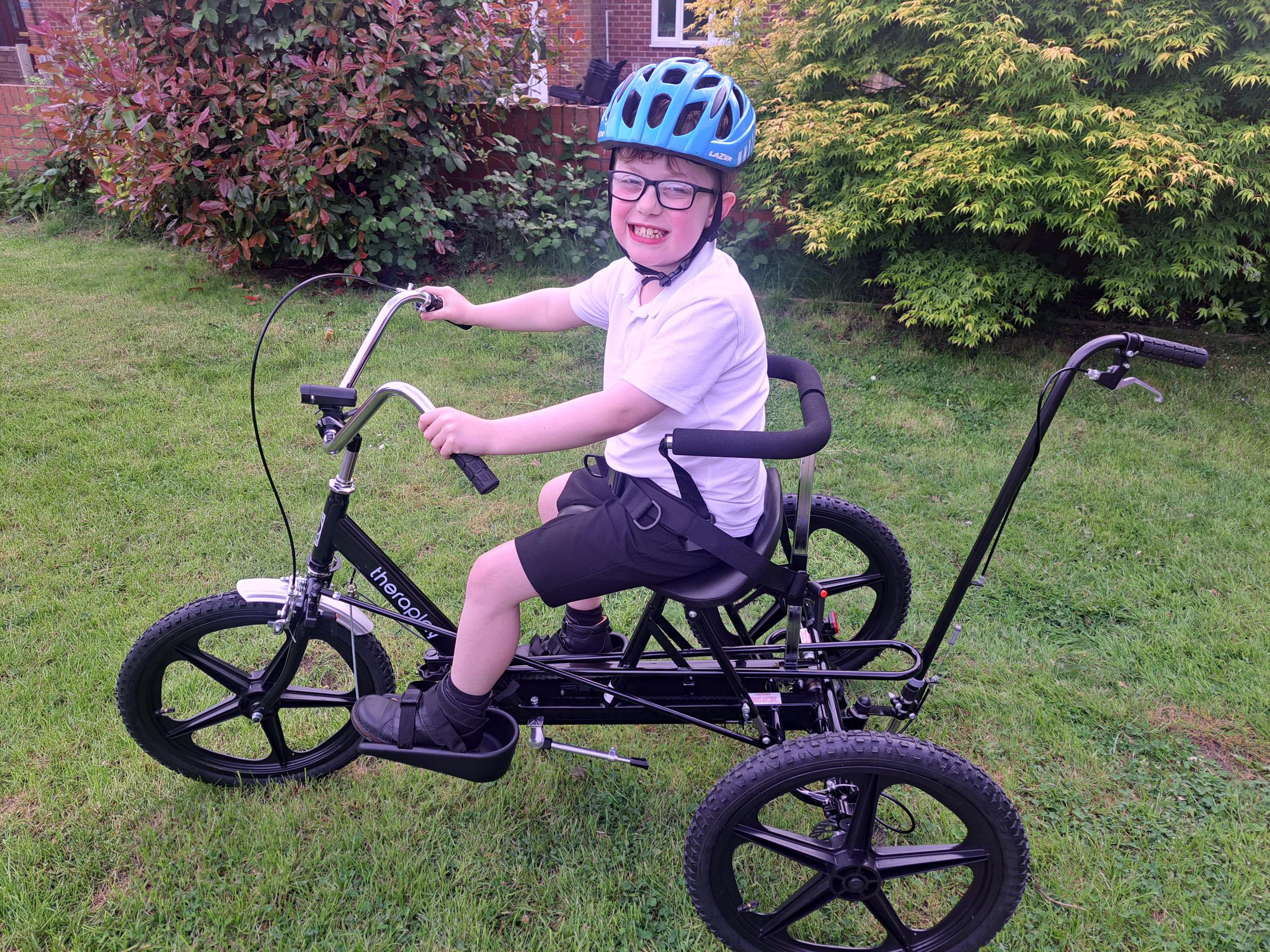 Boy riding trike smiling wearing helmet and school uniform