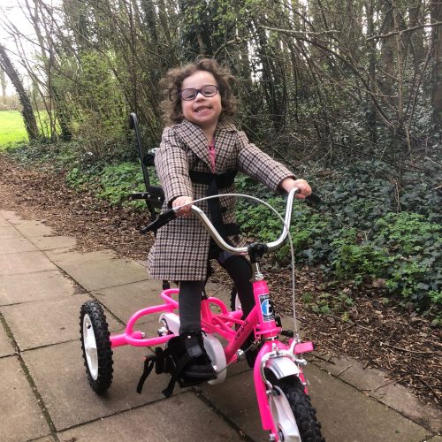 girl in wintery coat on a pink trike smiling in a park